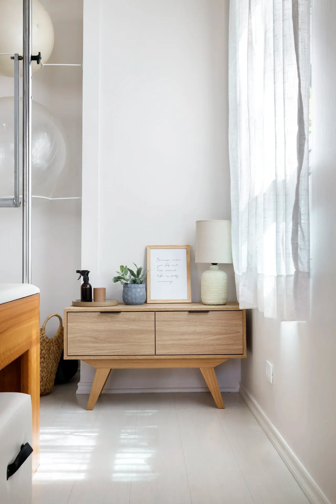 Criado-mudo de madeira com luminária, planta e objetos decorativos junto à janela