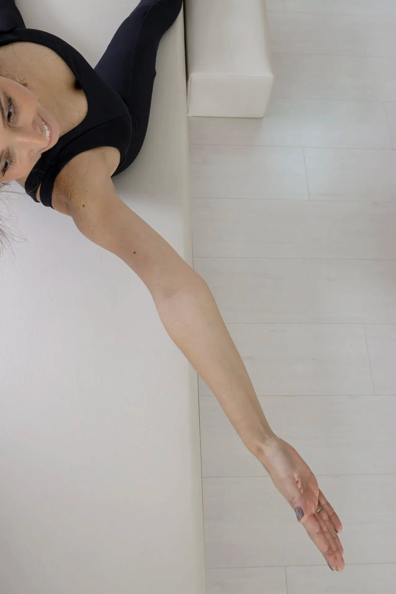 Detalhe artístico de aluna deitada com braço estendido no chão branco