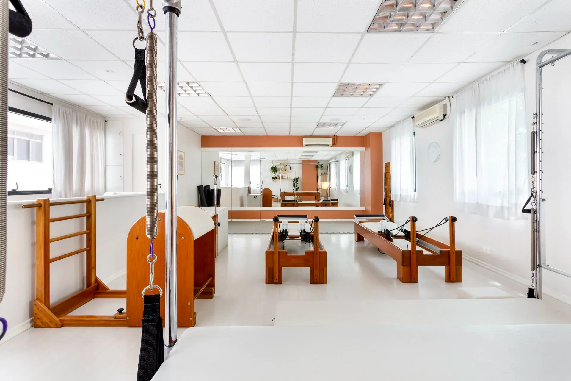 Vista lateral da sala com reformers, barrel e espelhos ao fundo