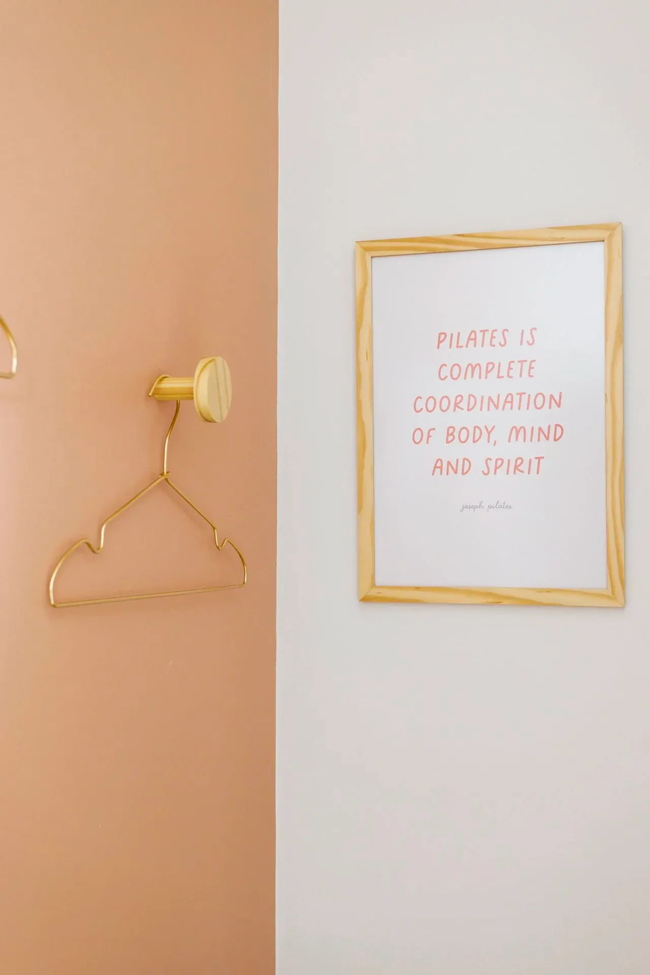 Vestiário com cabide dourado e quadro com citação de Joseph Pilates na parede